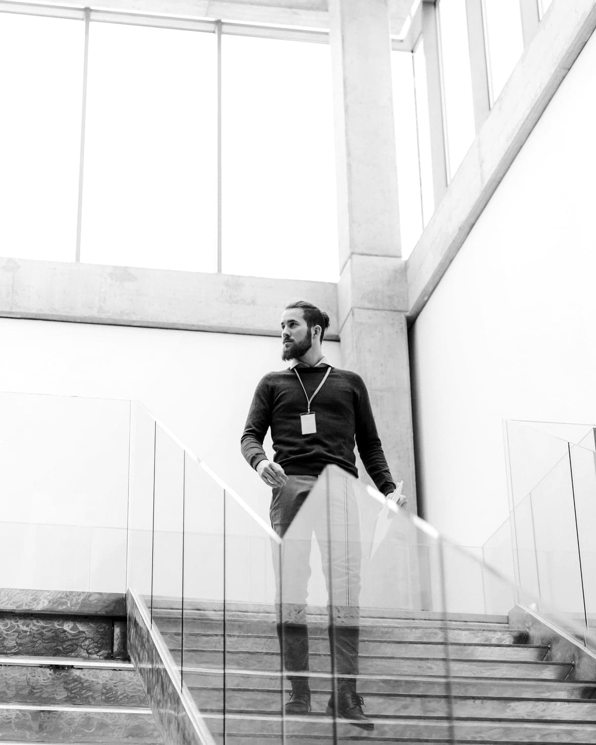 A man with a lanyard stands at the top of a glass stairway, looking out across the space