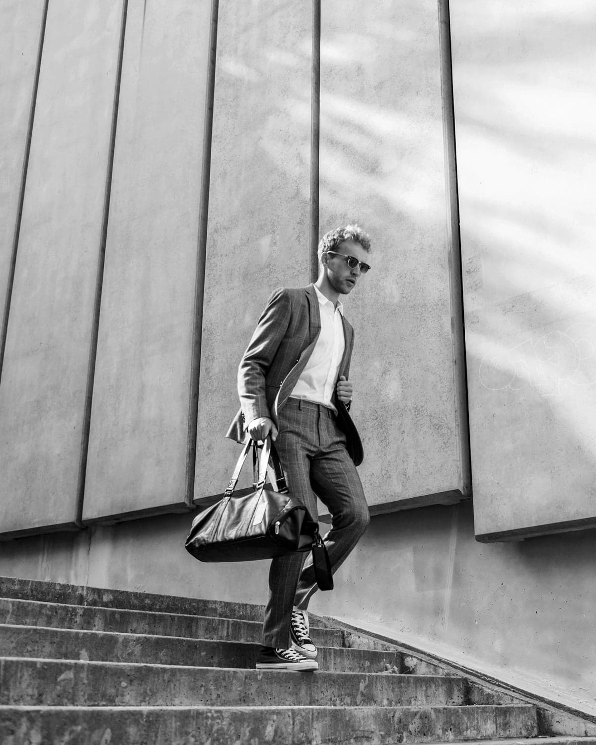 A man in sunglasses strides down concrete steps with a holdall in his hand