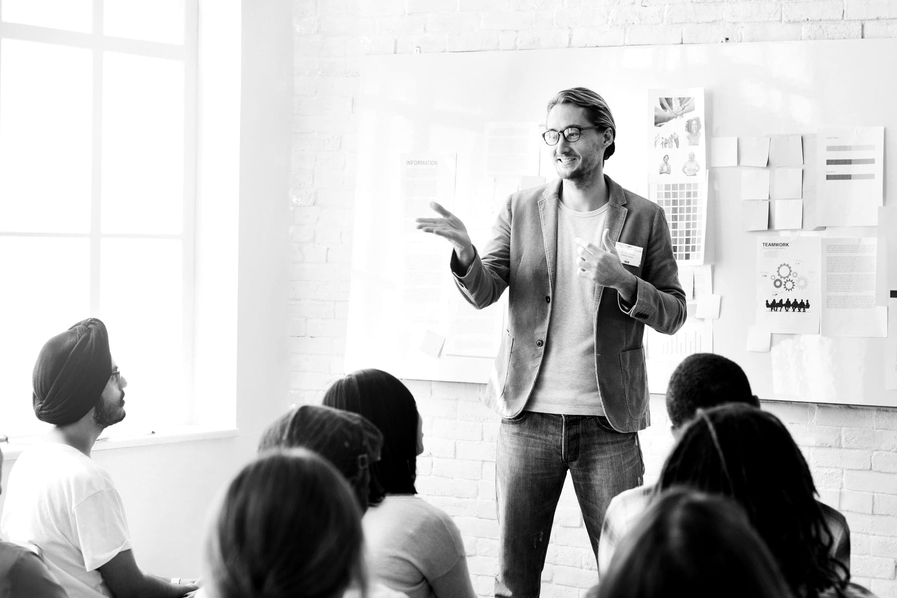 A facilitator talks with a seated group in front of a wall of notes