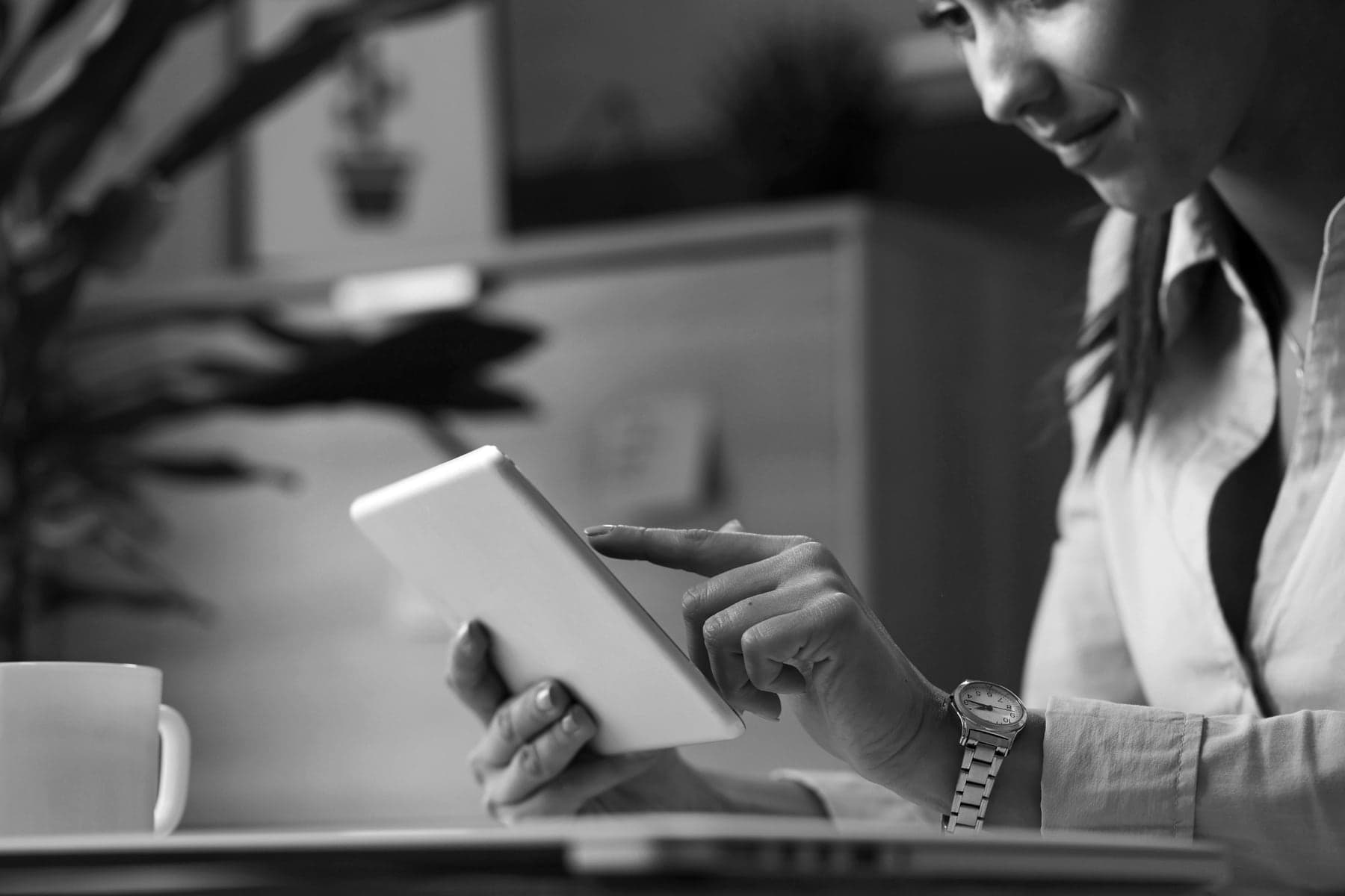 A woman smiles as she reads something on a tablet at her desk